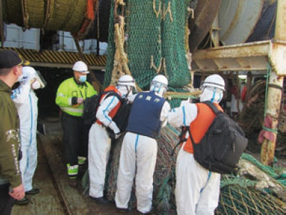 防護服を着て、外国漁船への立入検査を行う漁業監督官