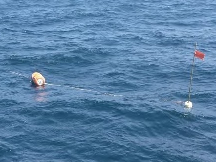 海上に浮かぶオレンジ色で円柱状の浮きと旗付きの白い浮き